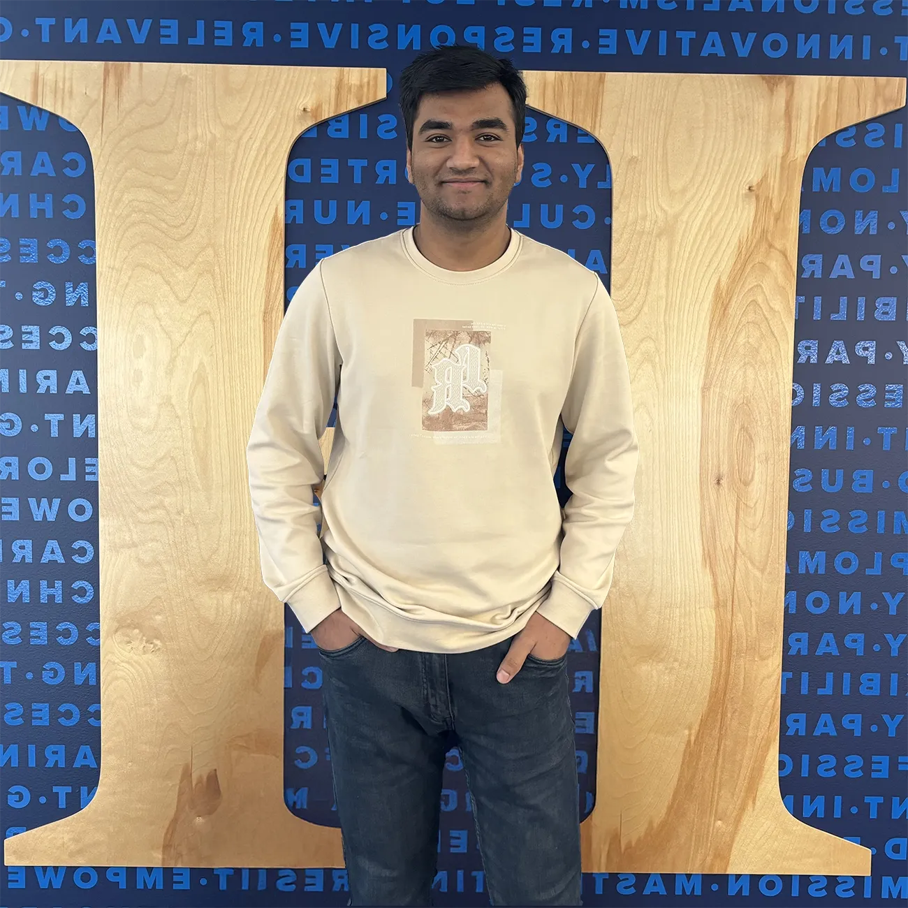 International student smiling and posing in front of a Herzing University wall with the university’s logo and motivational words in the background.